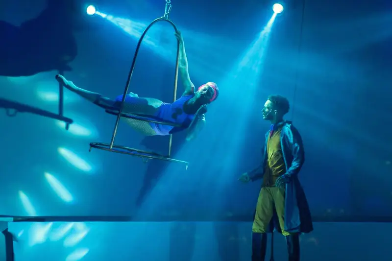 Acrobata em aparelho aéreo sob luzes azuis durante espetáculo no palco