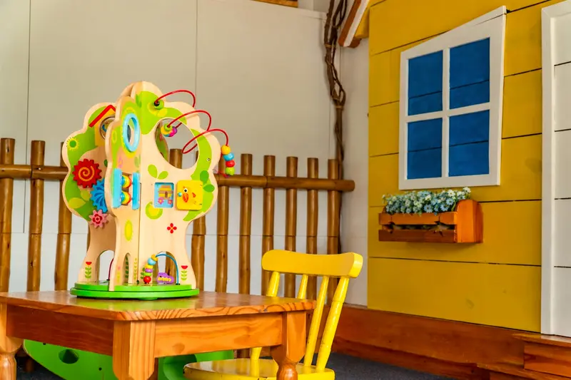 Espaço dos bebês com brinquedo educativo de madeira, cadeirinha e casinha amarela