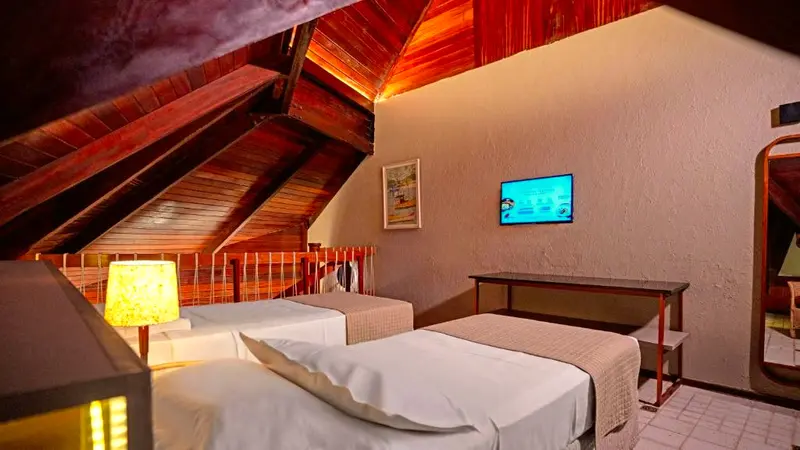 Mezanino com duas camas de solteiro, TV e teto inclinado de madeira