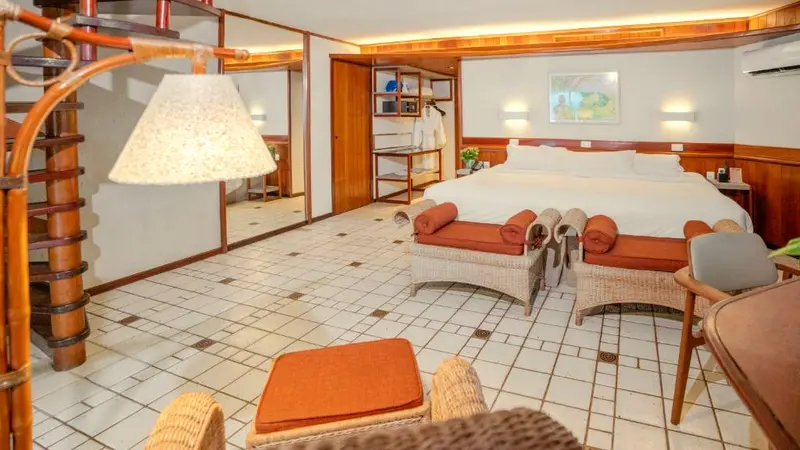 Quarto do bangalô com cama king, dois pufes e escada caracol de madeira