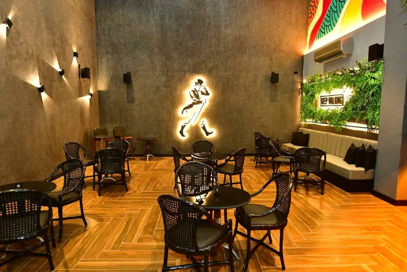 Salão de bar com mesas, cadeiras pretas e iluminação baixa