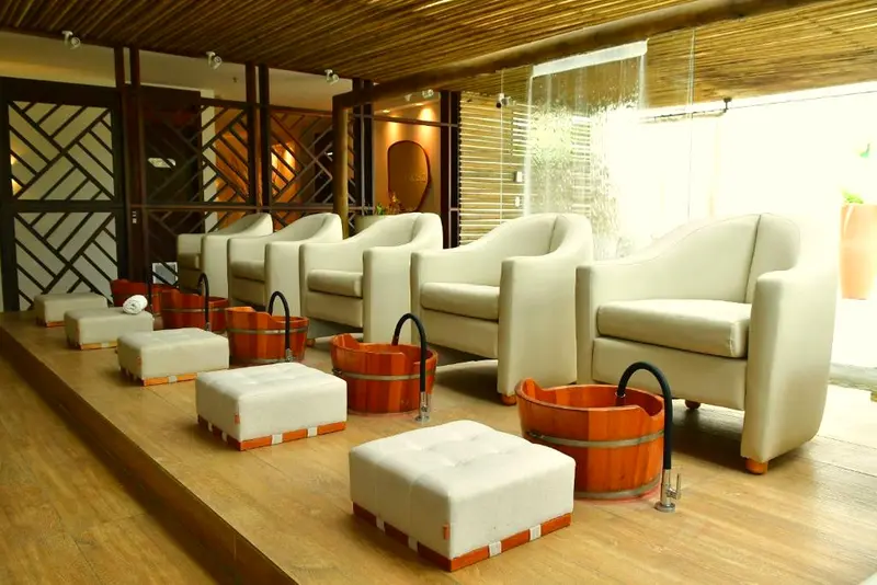 Espaço do spa com poltronas brancas, pufes e bacias de madeira para os pés