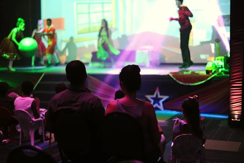 Apresentação no palco com bailarinos e luzes coloridas, vista da plateia