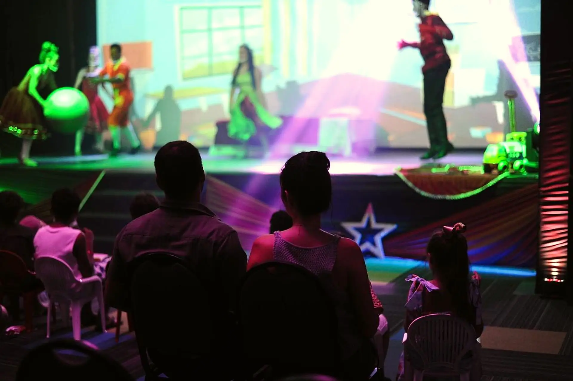 Apresentação no palco com bailarinos e luzes coloridas, vista da plateia