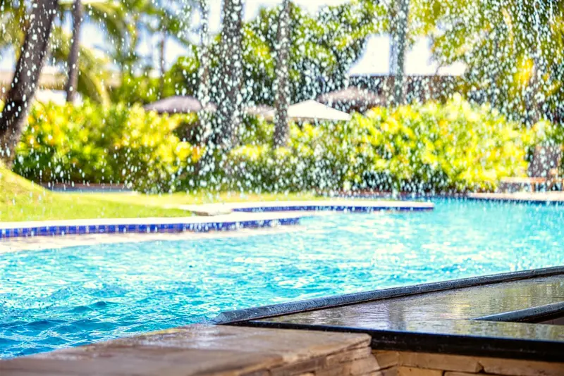 Jatos d’água caindo na piscina, com jardim ao fundo