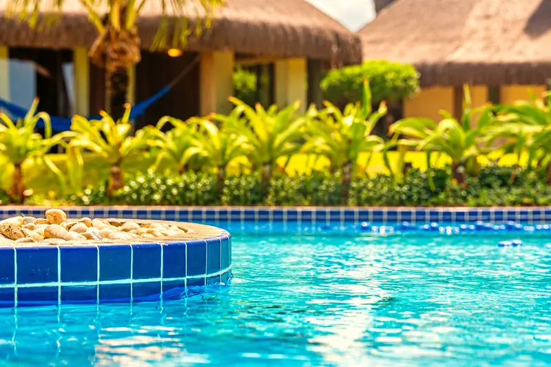 Piscina de hidromassagem cercada de folhagens e bangalôs de palha