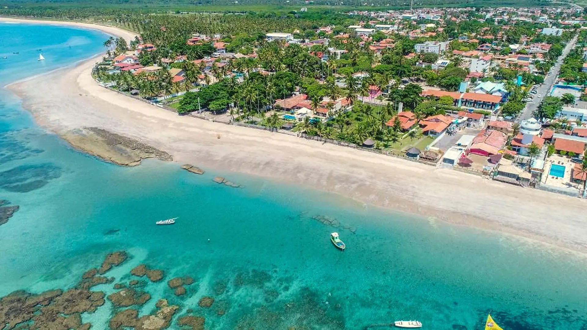 Vista aérea de um trecho do litoral com arrecifes, águas claras e casas entre a vegetação