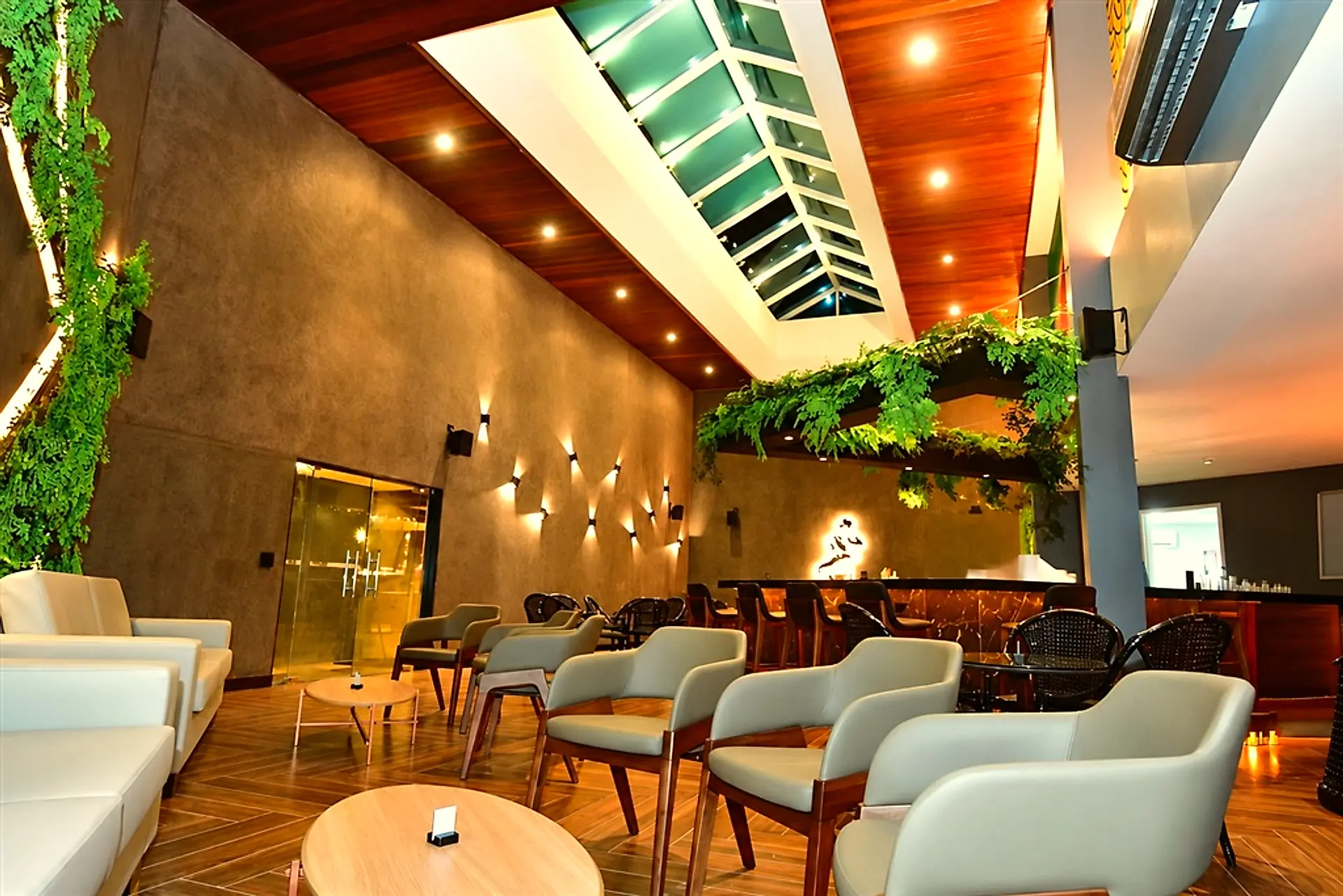 Lounge do lobby com poltronas claras, balcão de bar e teto de madeira