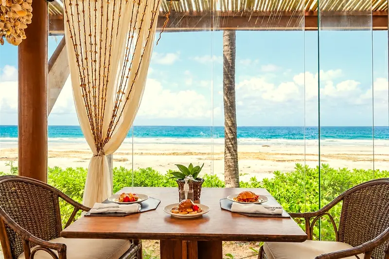 Mesa posta de frente para a praia, com cortinas e a areia ao fundo