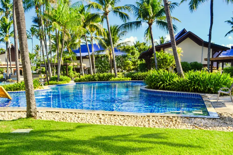 Piscina entre jardins e bangalôs de telhado azul