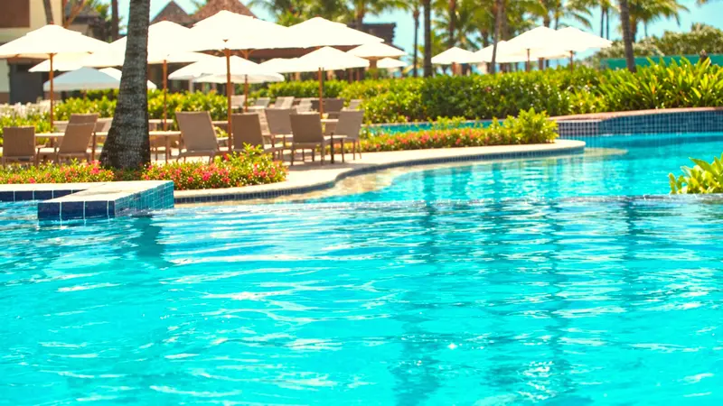 Piscina sinuosa de água azul com guarda-sóis e espreguiçadeiras ao redor
