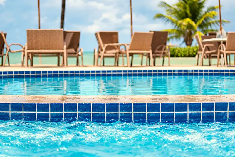 Piscina com cadeiras na borda e o mar ao fundo