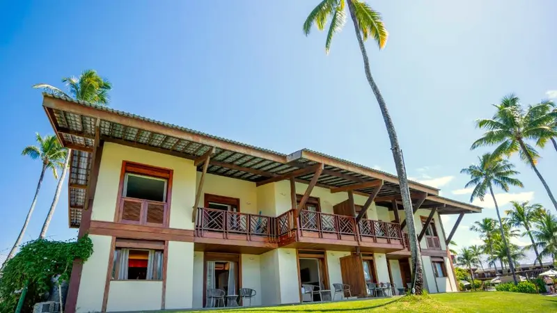 Prédio de apartamentos de dois andares com varandas de madeira entre coqueiros