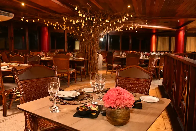 Salão de restaurante com mesas postas, flores e luzes no teto