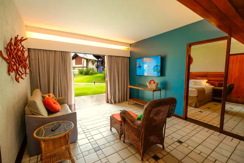 Sala da Suíte com sofá, poltrona de vime e porta aberta para o jardim