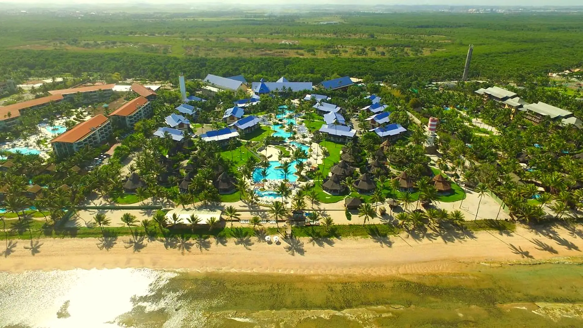Vista aérea do resort à beira-mar, com a faixa de areia, os jardins e as piscinas entre os coqueiros